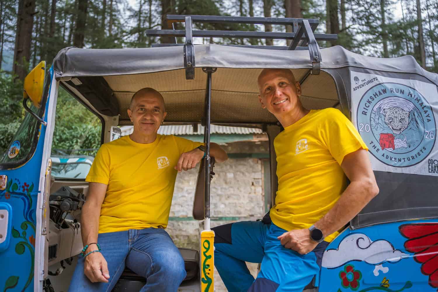 Due uomini sorridenti in un tuk-tuk decorato in un'area boschiva.