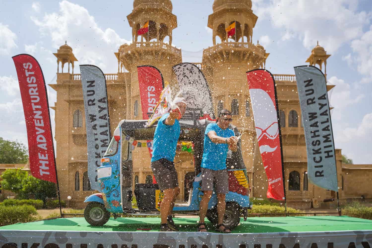 Due persone festeggiano con acqua davanti a un palazzo storico in un evento di corsa.
